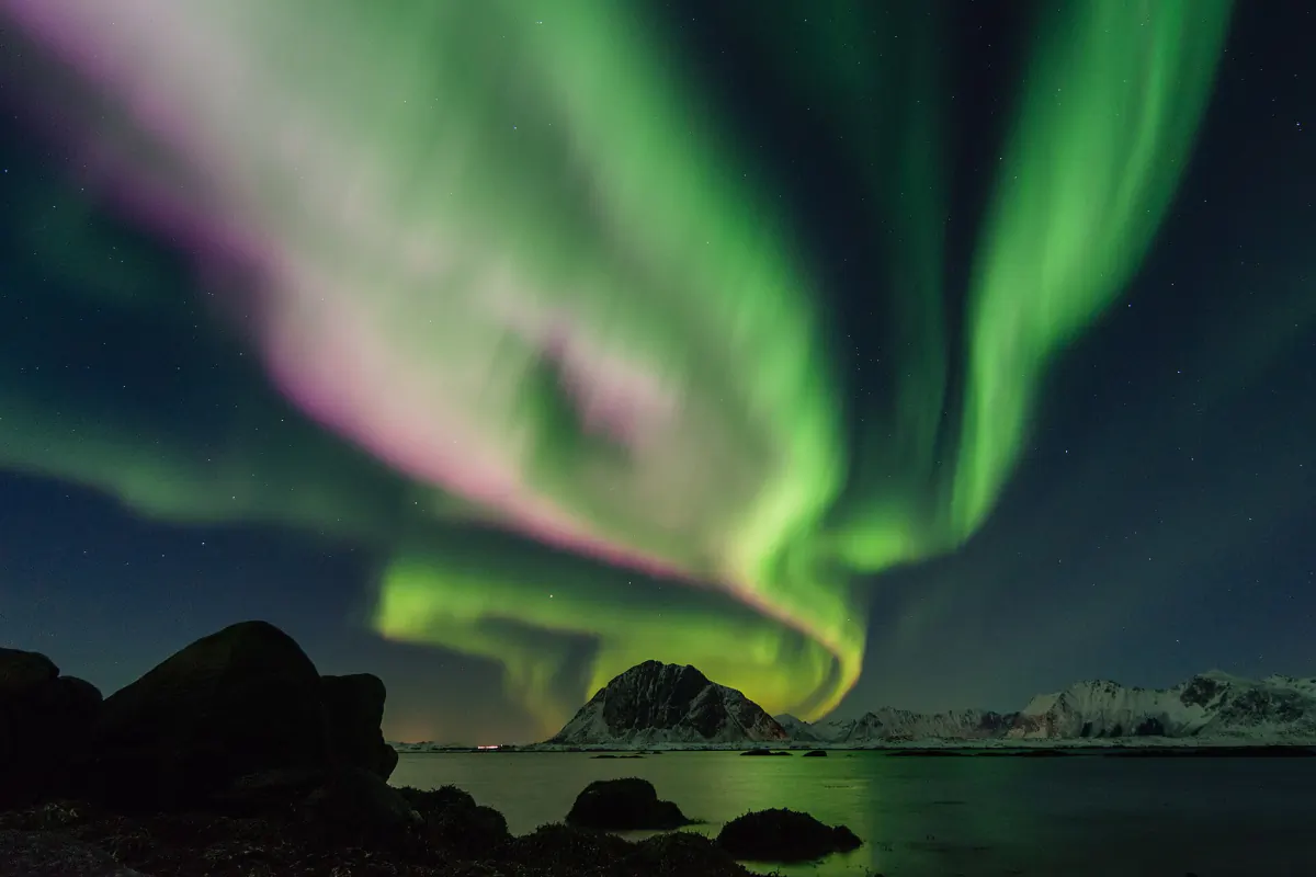 Green aurora arc over the mountains and shoreline at Flakstad in Lofoten, Norway
